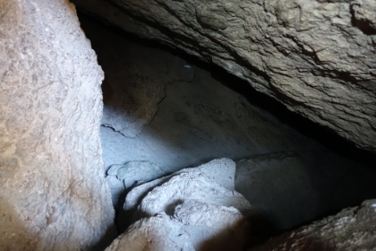 Climbing down into a deeper area of the cave. You can see a little white reflective arrow painted on the rock below. The "trail" goes down and to the right into the pitch black.